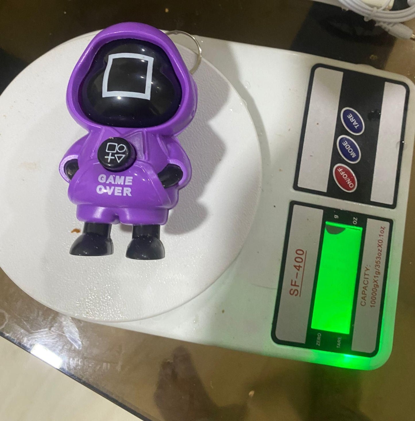 Toy figure Squid Game in a red hood with 'GAME OVER' text on a dark background